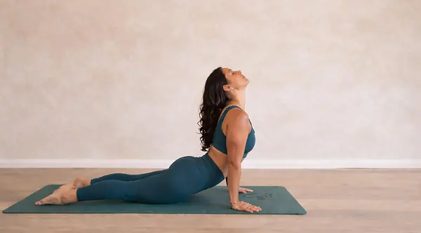 A student holding upward-facing dog on a mat in a sunlit studio