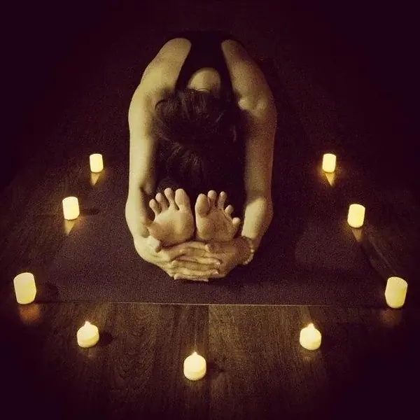 A student folded forward on a mat surrounded by candlelight in a dim studio